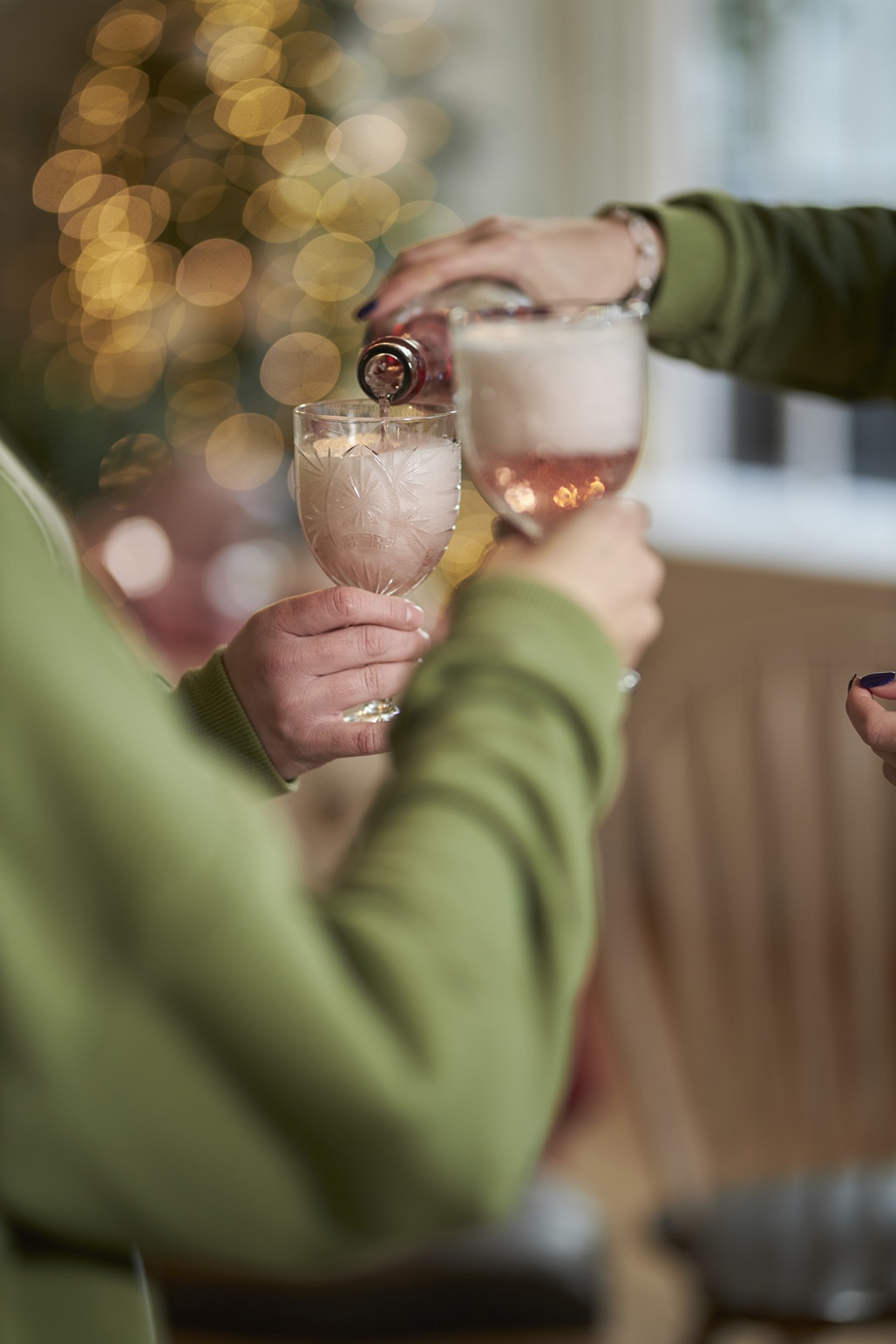 Grüne Ärmel und Hände von Frauen mit Gläsern darin, die miteinander mit einem Sekt an einem Mädelsabend anstoßen.